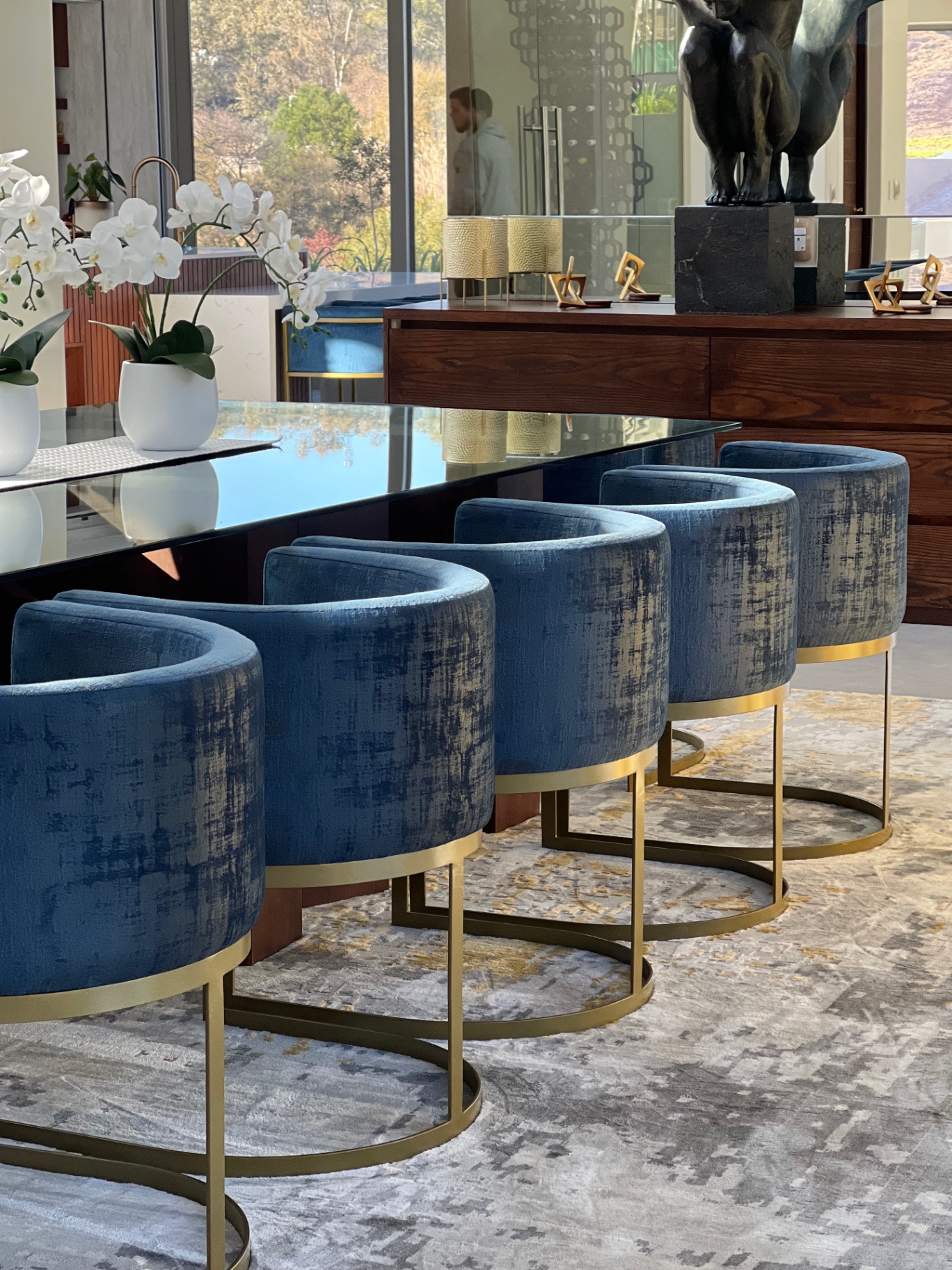 Bespoke velvet tub dining chairs with brass bases around a smoked glass table