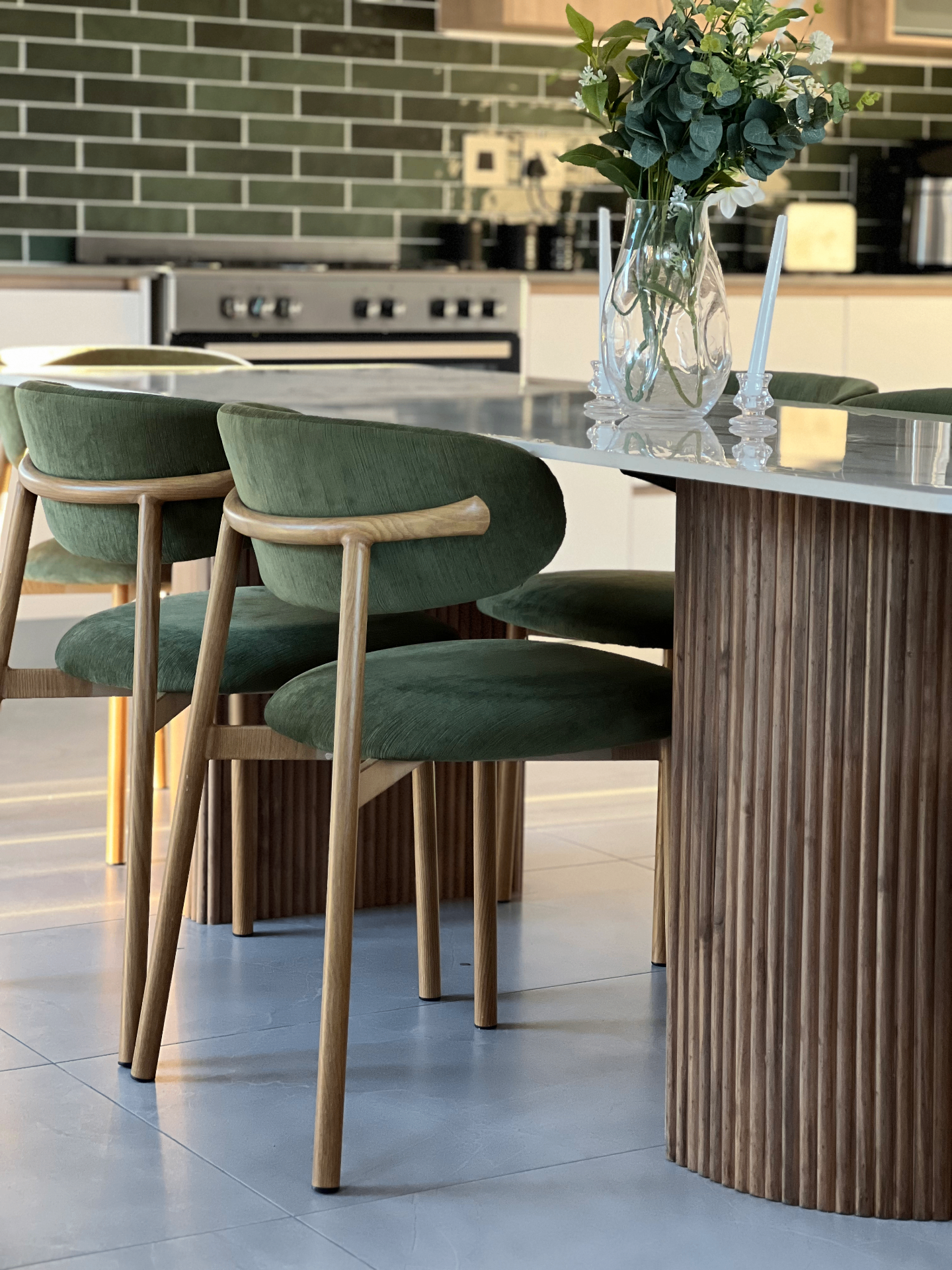 Bespoke green velvet dining chairs with timber frames around a marble fluted-base table